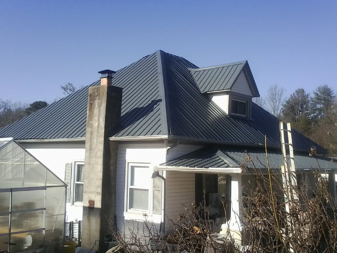 Dark blue standing seam metal roof on a white farmhouse with dormer — Slate & Tile Roof Repair by Roofing Brothers in Ketchum