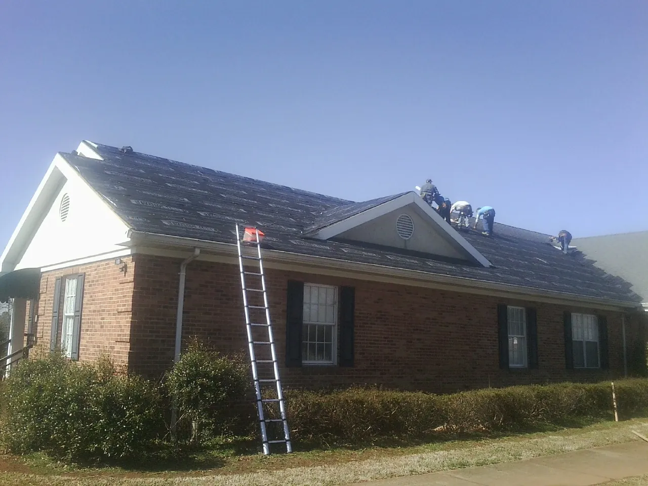 Crew tearing shingles off a brick ranch roof with a ladder set — Emergency Roof Repair work by our crew in Ketchum