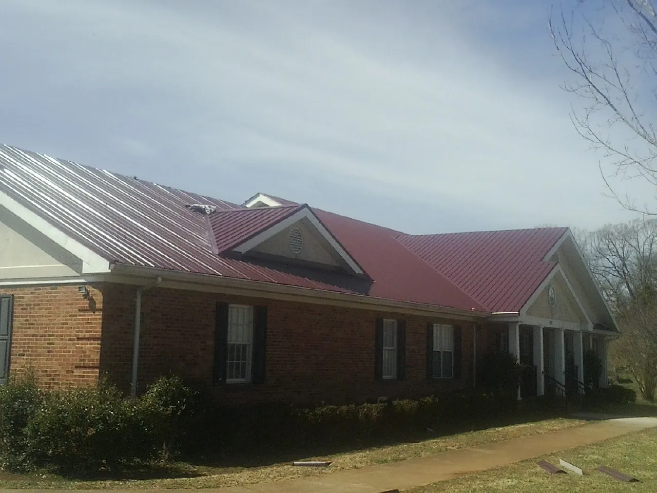 Red metal roof with gabled entries on a long brick building, from a Hail Damage Roof Repair job in Ketchum