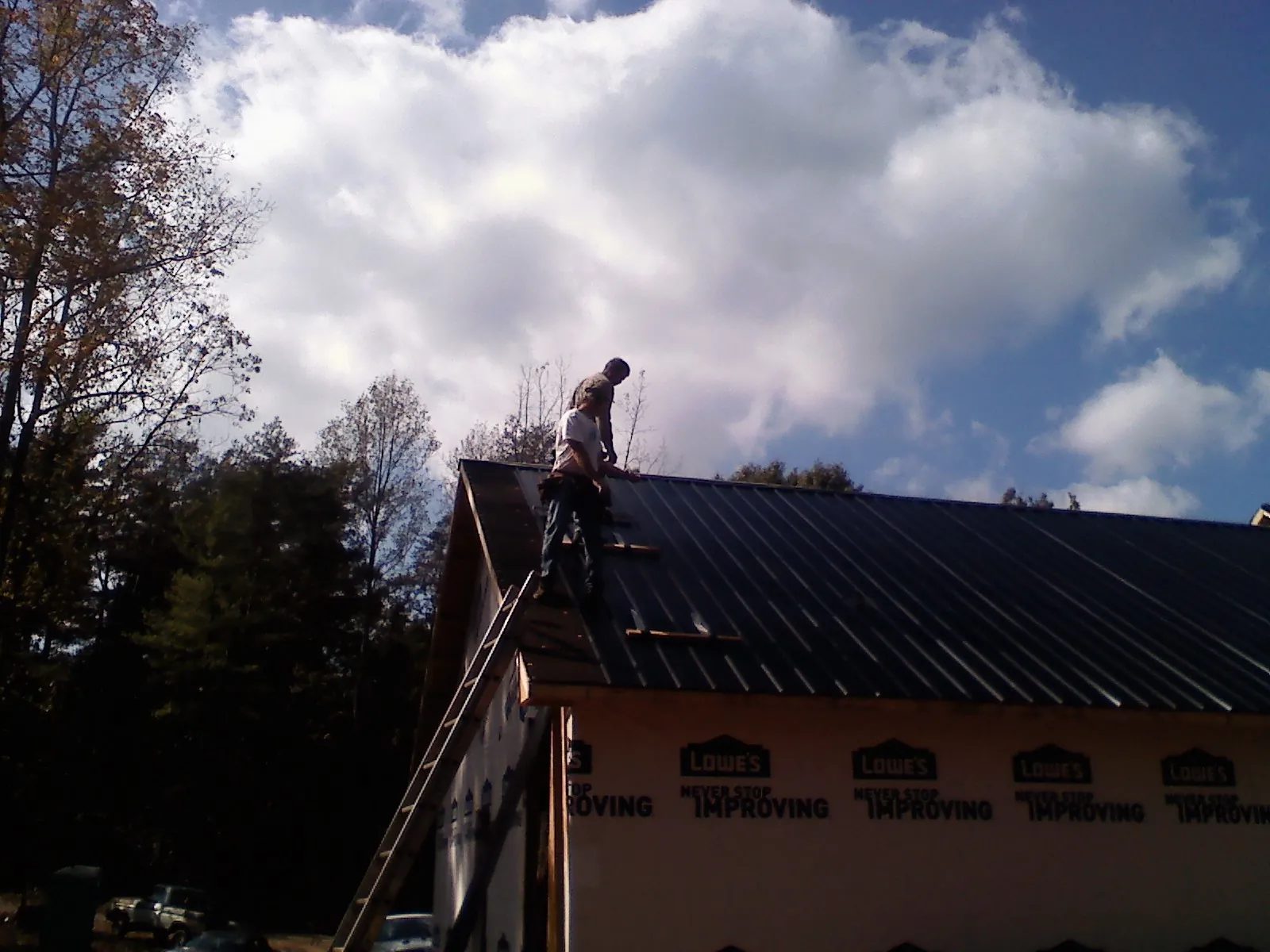 Roofer fastening dark metal panels high against a cloudy sky, from a Roof Inspection job in Ketchum