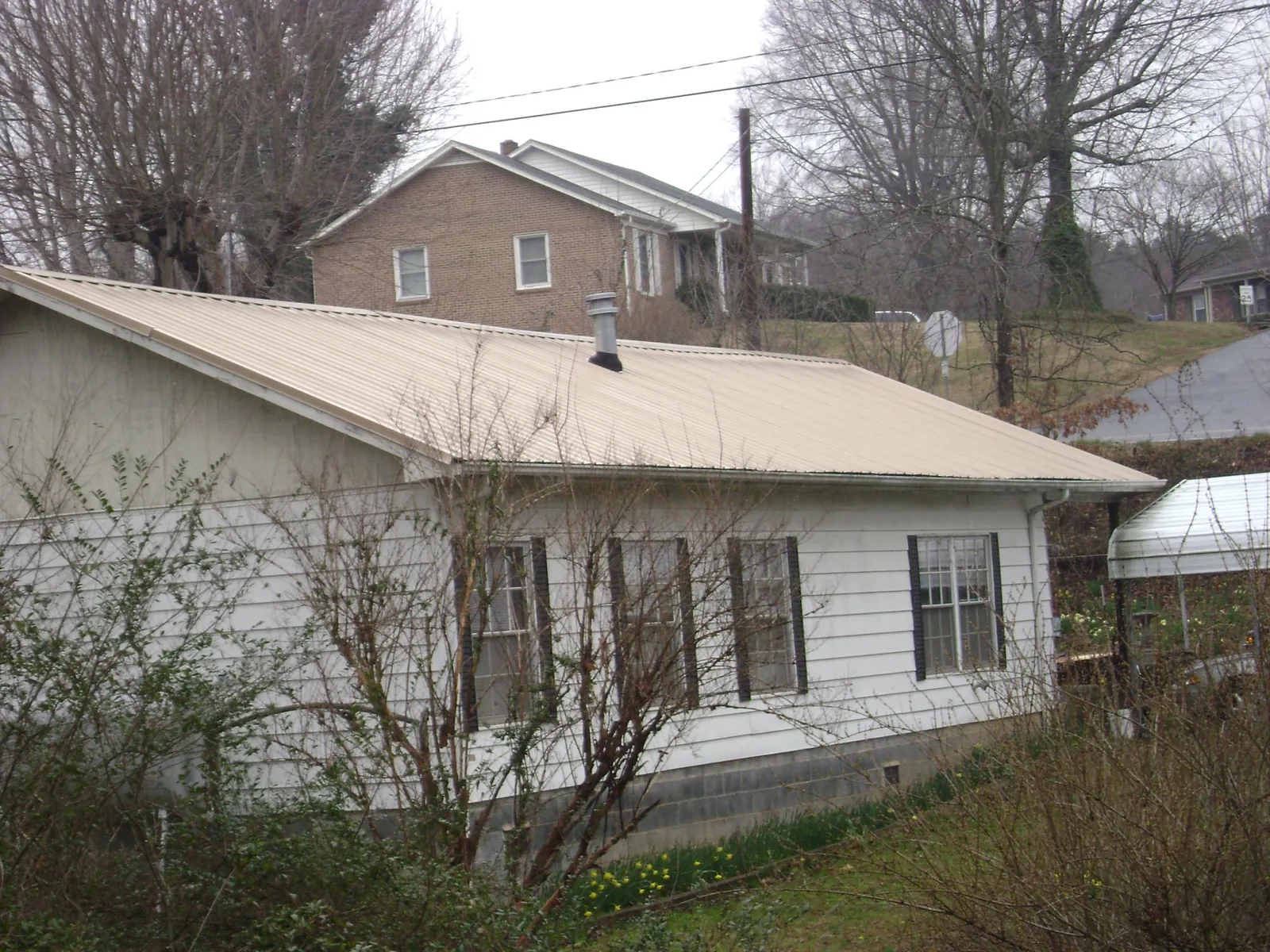 Tan metal roof on a white sided house set into a hillside — Commercial Roofing by Roofing Brothers in Ketchum